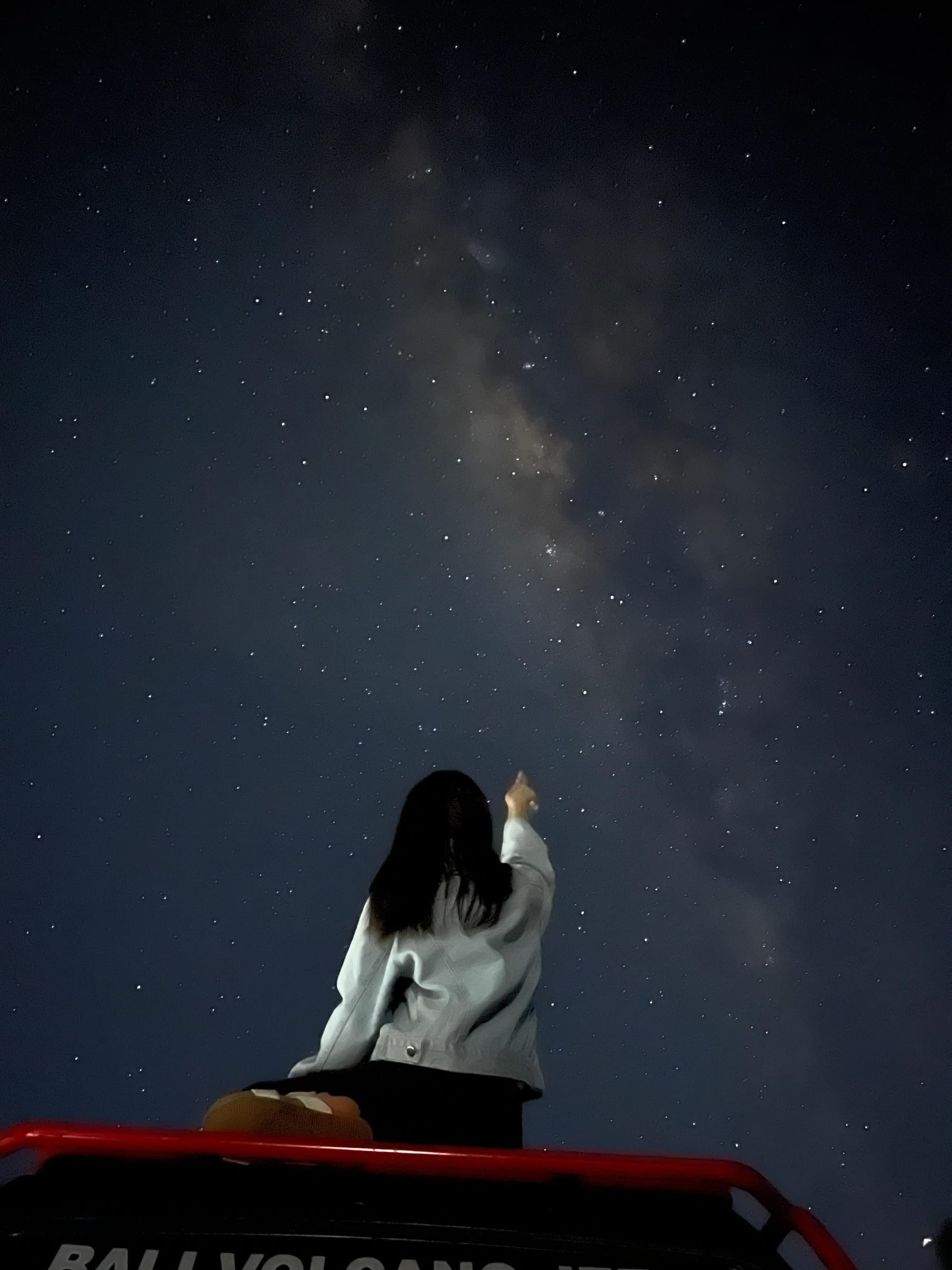 A guest on a jeep roof in the dark, pointing up at the Milky Way over the caldera