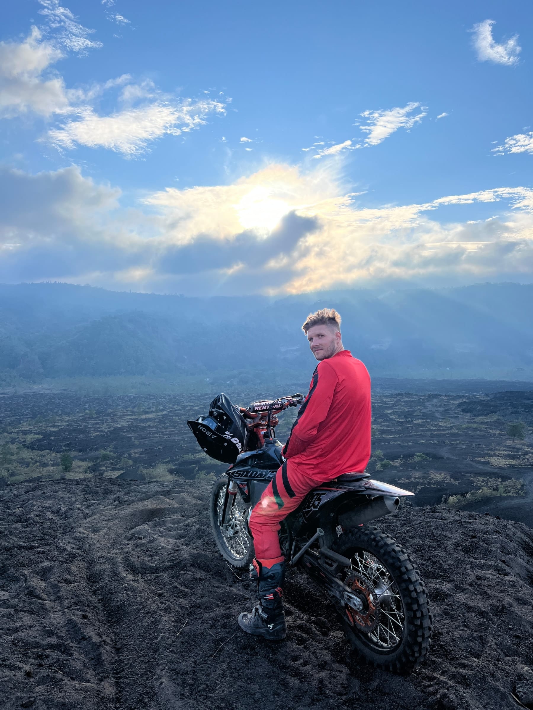 A rider on a 250cc bike out on the black lava field, sunbeams breaking over the hills behind him