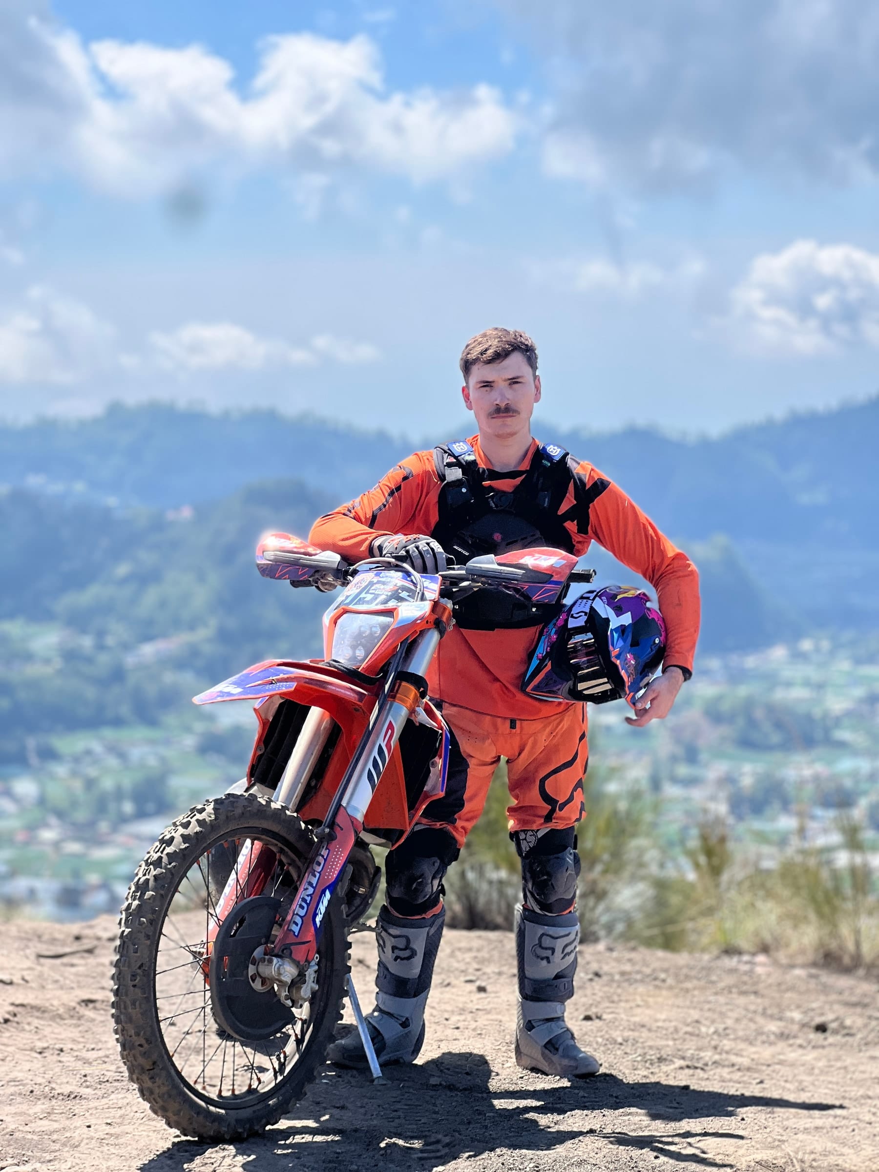 A rider in full body armour standing with his 250cc bike above the caldera, Lake Batur behind him