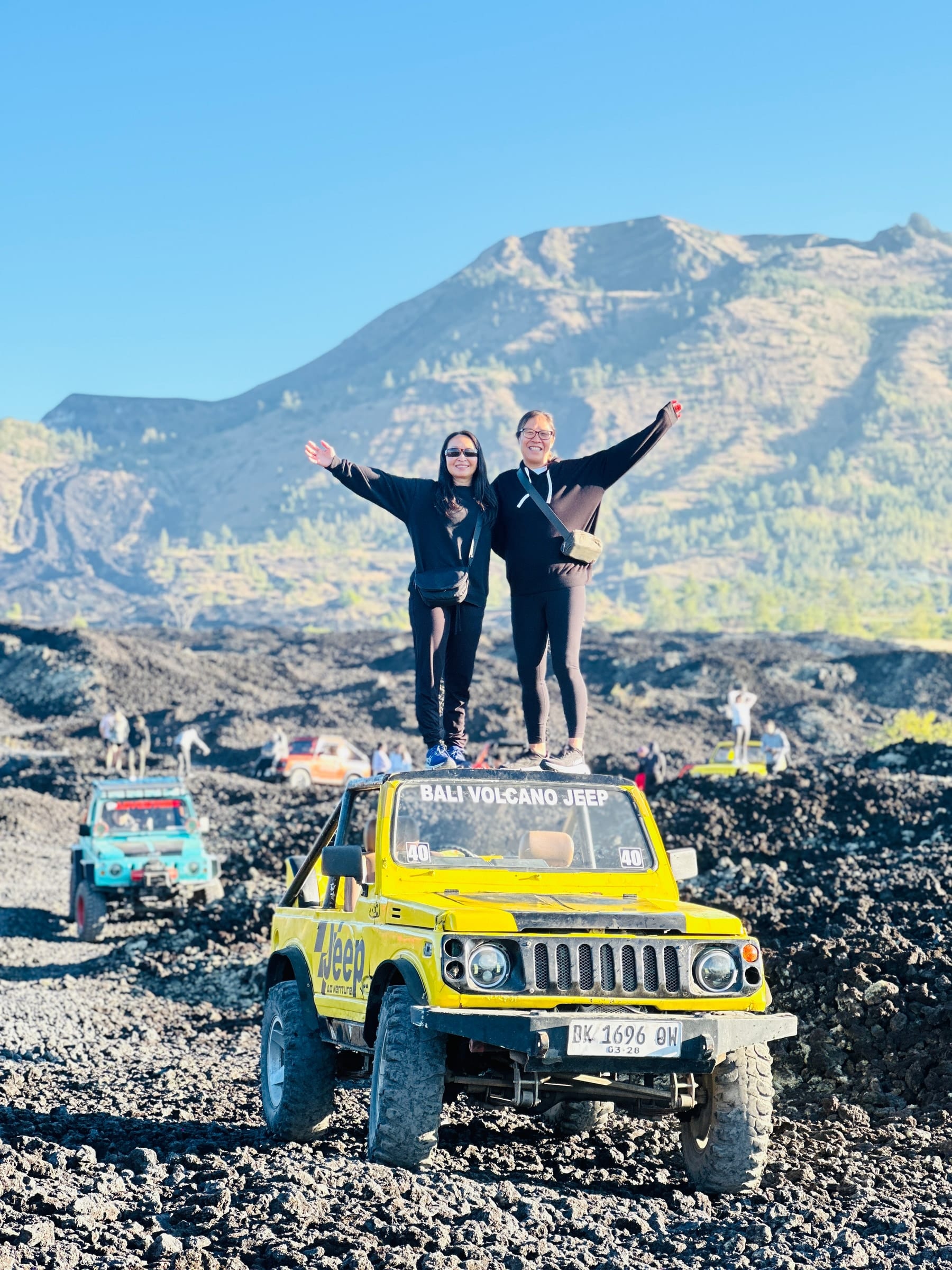 A couple standing on a jeep bonnet with their arms out, the Batur cone behind them