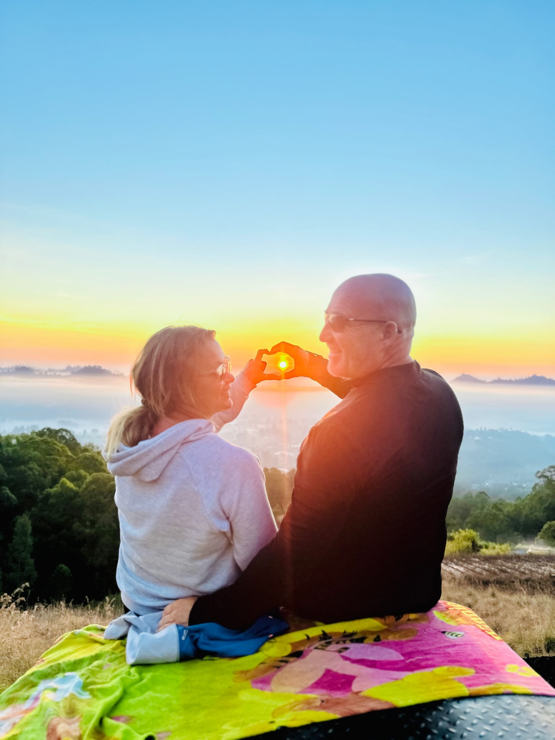 A couple framing the rising sun between their hands from the roof of a jeep