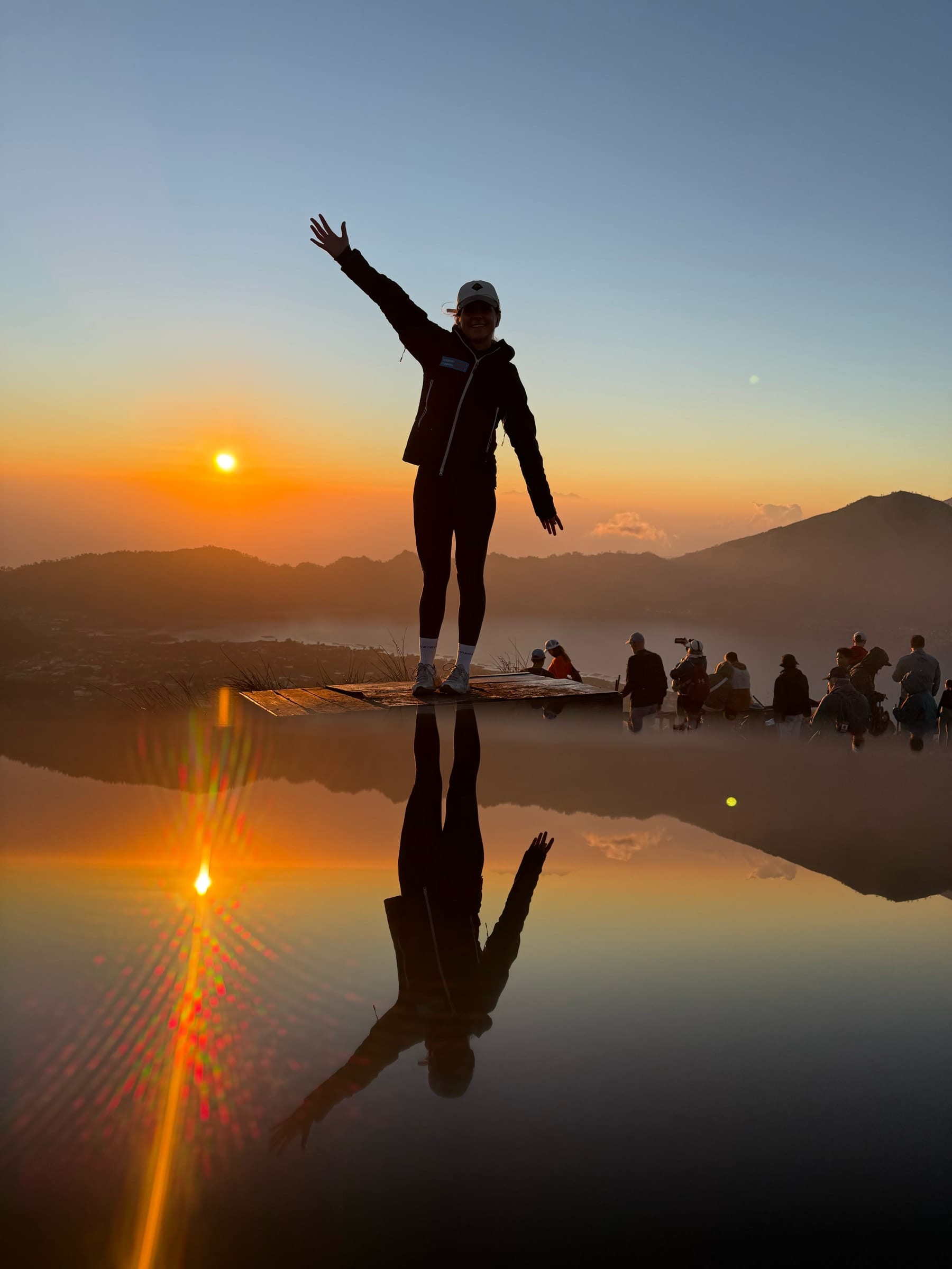 A trekker reflected in the summit rain pool as the sun comes up over Lake Batur